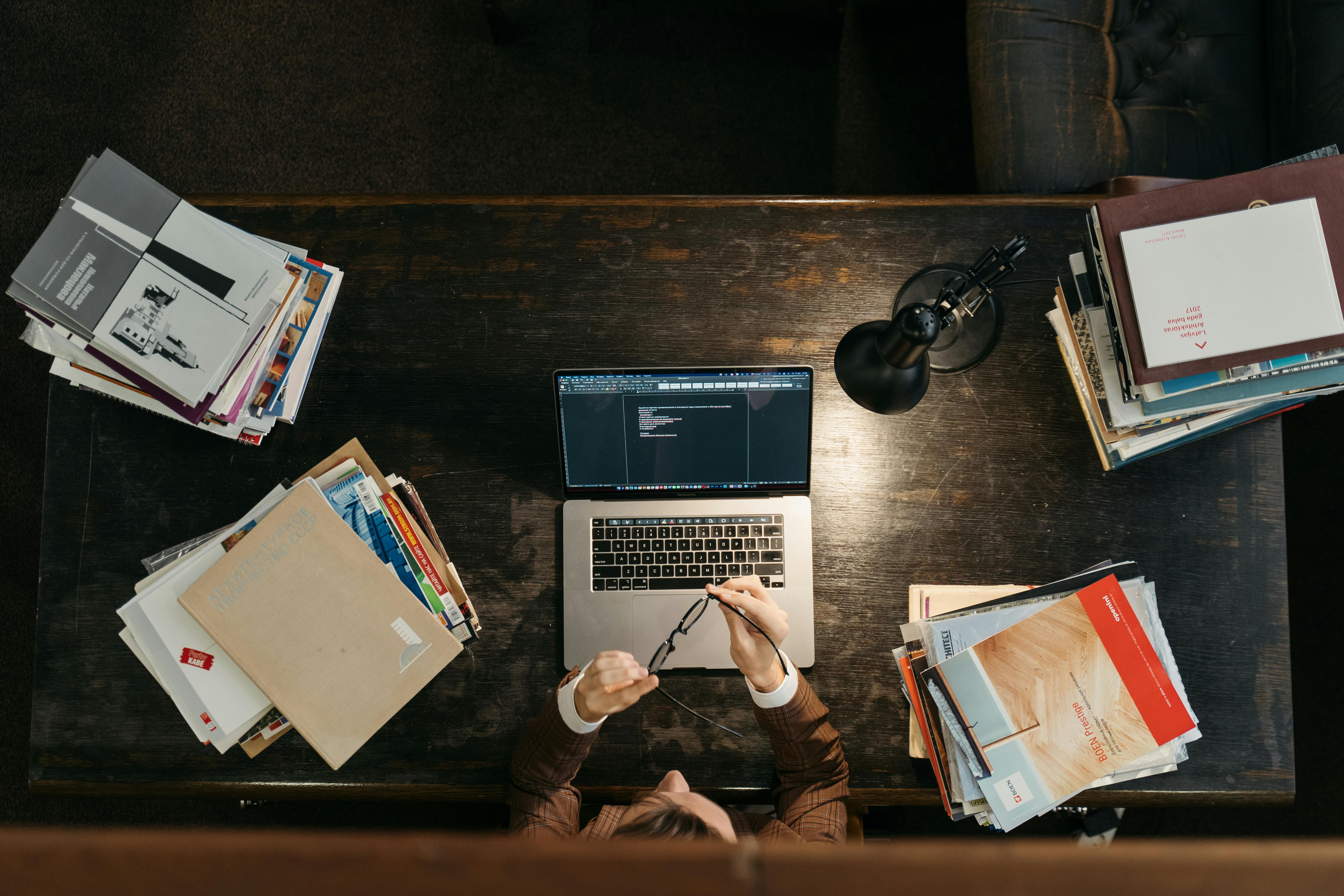 High-angle shot of a busy desk with books, laptop, and lamp, illustrating focused academia.
